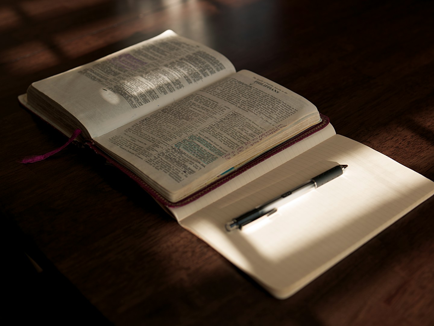 An open Bible with a notebook and pen in warm light.